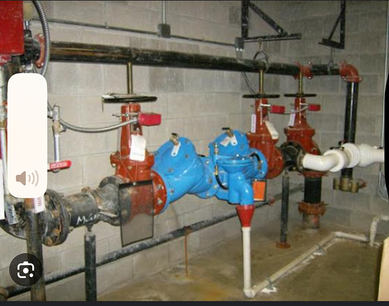 Industrial plumbing system with red and blue valves and pipes mounted on a concrete wall.