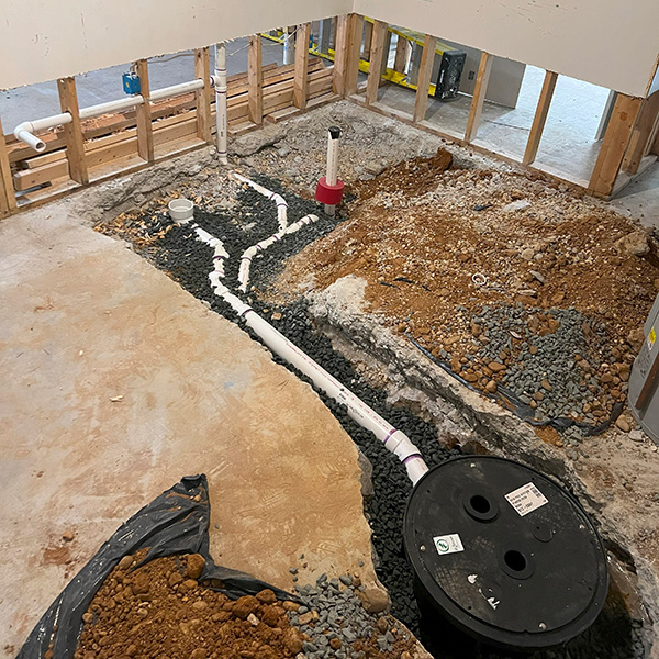Basement construction site with exposed plumbing, drainage system, gravel, and bare walls, showing structural work in progress.