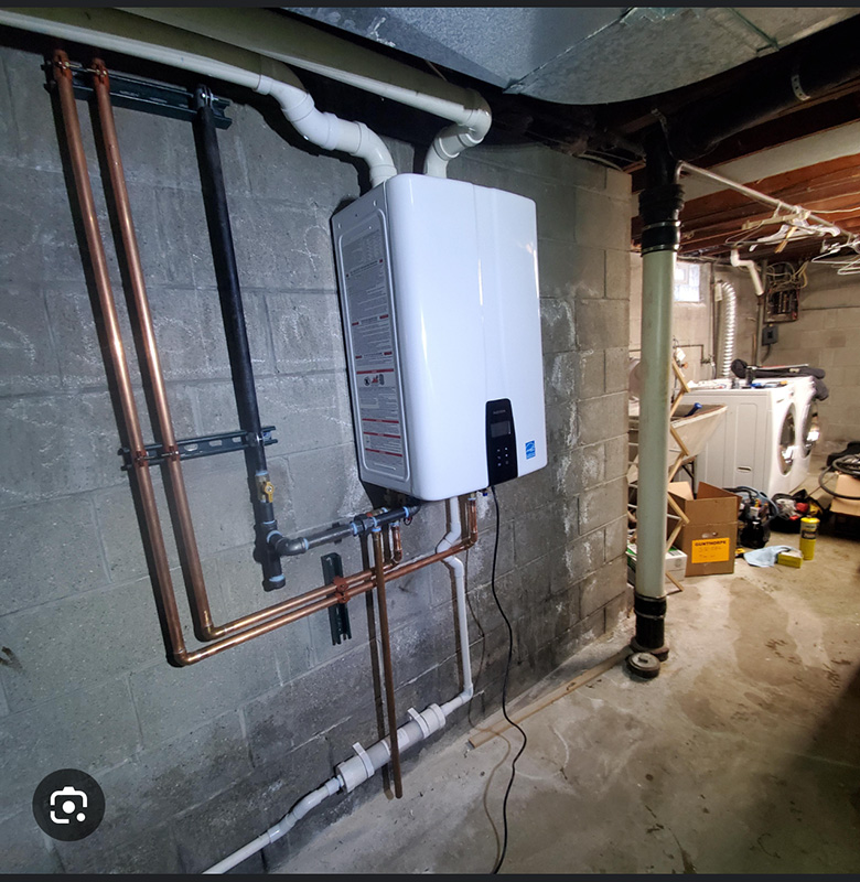 Basement with mounted tankless water heater, exposed copper pipes, concrete walls, and laundry machines in the background.